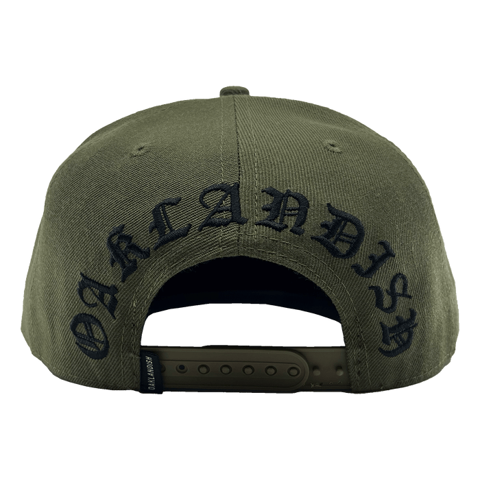 The Old English Aft Snapback by Oaklandish, showcased from the rear, features an adjustable strap and the word "OAKLANDISH" embroidered in a black Gothic-style font. The green cap includes a small black tag with white text near the strap and an Oaklandish tree logo. The fabric texture is also visible, highlighting its durable material.