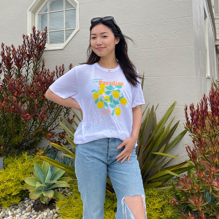 Woman posing outdoors wearing the Paradiso T-Shirt with bright lemon design and casual ripped jeans