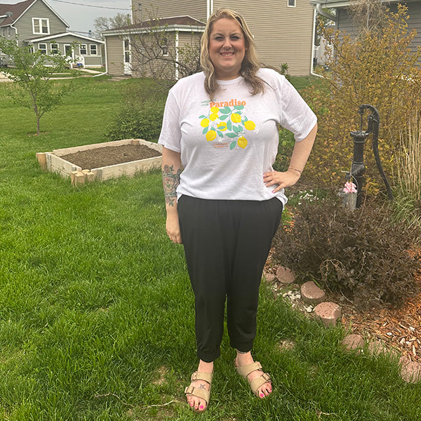 Person standing outdoors wearing the Paradiso T-Shirt with yellow lemon cluster graphic and casual black pants
