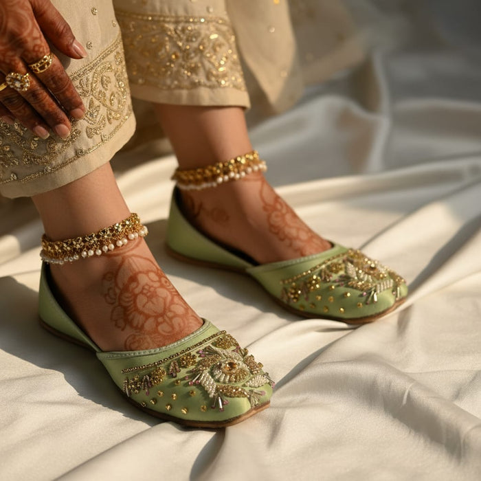 Green embroidered shoes worn with gold jewelry on a light fabric background