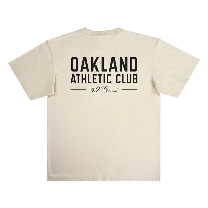 Beige Prestigious Tee by OAC shown flat, crafted from heavy-weight cotton, featuring large black “OAKLAND ATHLETIC CLUB” text in bold on the back, with “59 Grand” in cursive beneath and two horizontal lines framing the lower text.