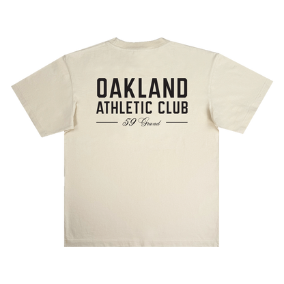 Beige Prestigious Tee by OAC shown flat, crafted from heavy-weight cotton, featuring large black “OAKLAND ATHLETIC CLUB” text in bold on the back, with “59 Grand” in cursive beneath and two horizontal lines framing the lower text.