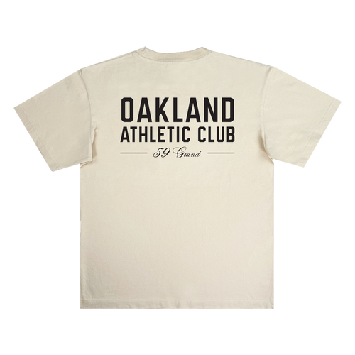 Beige Prestigious Tee by OAC shown flat, crafted from heavy-weight cotton, featuring large black “OAKLAND ATHLETIC CLUB” text in bold on the back, with “59 Grand” in cursive beneath and two horizontal lines framing the lower text.