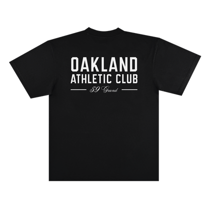 The Prestigious Tee by OAC is a black classic fit t-shirt made from heavyweight cotton, shown from the back against a plain white background. Centered on the shirt is bold white text that reads “OAKLAND ATHLETIC CLUB,” with smaller cursive lettering below that says “59 Grand.”.