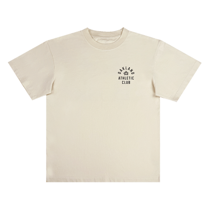 The Prestigious Tee by OAC is a classic fit, heavy-weight cotton t-shirt in plain off-white. It features “OAKLAND ATHLETIC CLUB” printed in black alongside a small laurel wreath graphic on the left chest. The shirt is displayed flat against a white background.