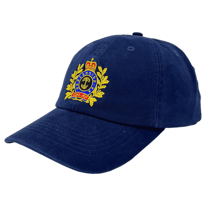 The Regal Crest Dad Hat by Oaklandish is a navy blue, 100% cotton hat with a detailed embroidered emblem on the front. The emblem features a golden crown at the top, a circular design with text below, and laurel leaves on either side. The visor is slightly curved and there’s an adjustable strap at the back for a perfect fit.
