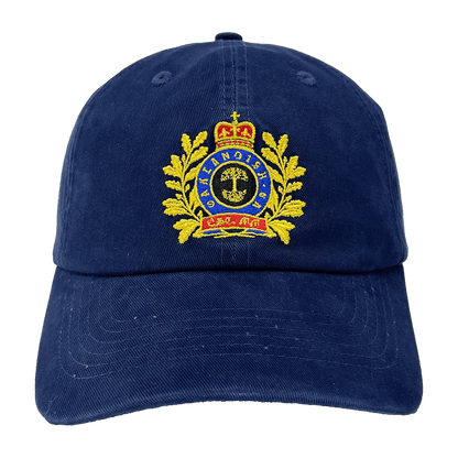 The Regal Crest Dad Hat by Oaklandish is a navy blue hat featuring an embroidered gold emblem on the front. The intricate design includes a crown at the top, gold laurel wreaths on either side, and a central shield with detailed symbols. Blue text is threaded within the emblem, framed by the wreaths. Made from 100% cotton, it also includes an adjustable strap for added comfort.