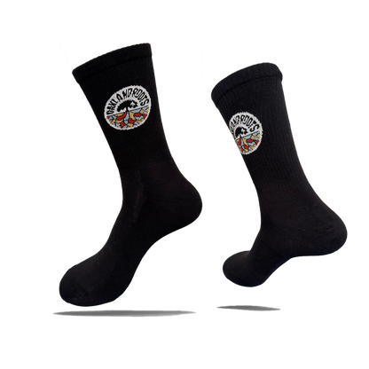 Two black cotton crew Roots SC Socks by Oakland Roots SC are shown against a white background. Each adult-sized sock features a round “NOMAD NOMADS” patch with colorful wings near the top and appears to float with shadows below.