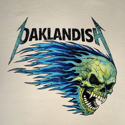 Sure! Here’s a rewritten version using your product data: The Sandman Tee by Oaklandish features bold black “Oaklandish” lettering with electric blue lightning bolts. Below the text, a vivid green skull with streaming blue flames is shown facing left, mouth open and baring sharp teeth with hollow eyes. Printed on a classic fit t-shirt, this striking design pops against the plain beige background.