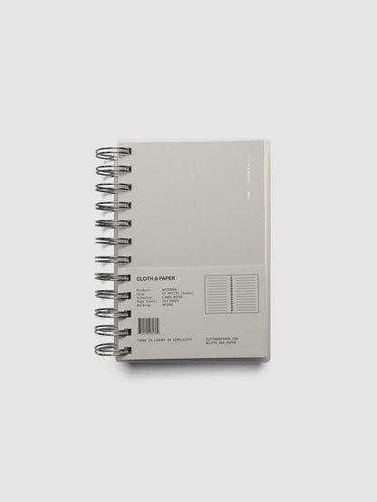 Spiral Notebook in size CP Petite and color Ash with Lined Note interior pages shown closed from the front with belly band.