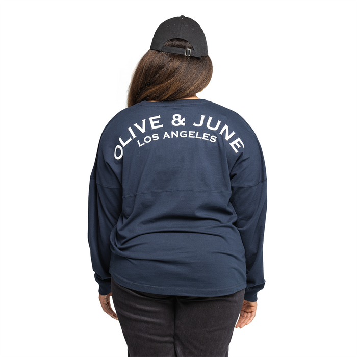 Back view of a navy Summer Sailor Long Sleeve Shirt with white Olive and June Los Angeles lettering worn with black cap