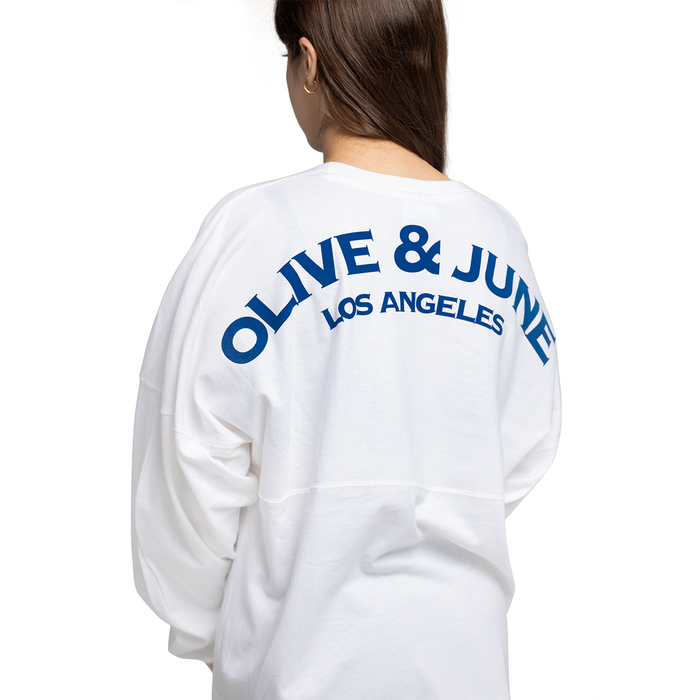 Back view of white Summer Sailor Long Sleeve Shirt with bold navy Olive & June Los Angeles lettering worn by model