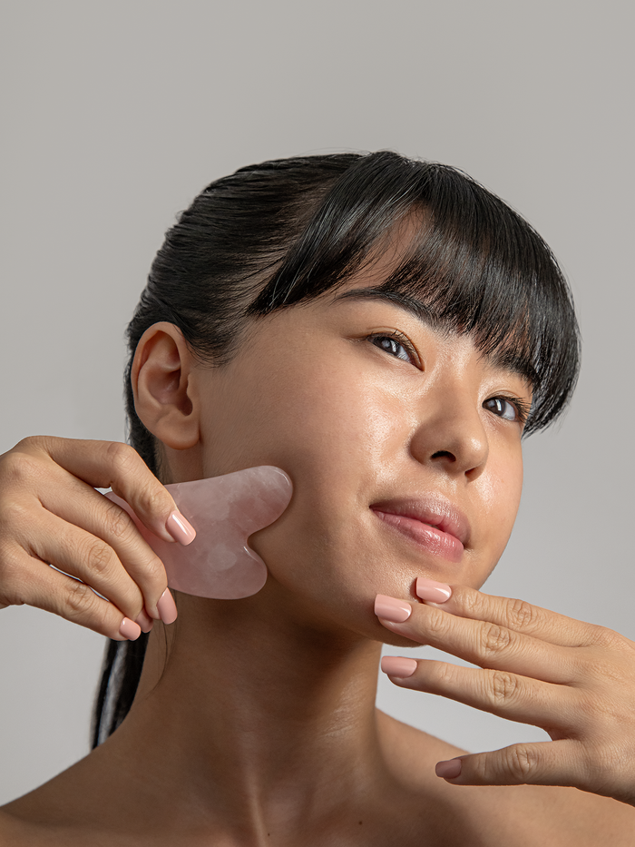 Woman using rose quartz gua sha lifting tool to sharpen jawline
