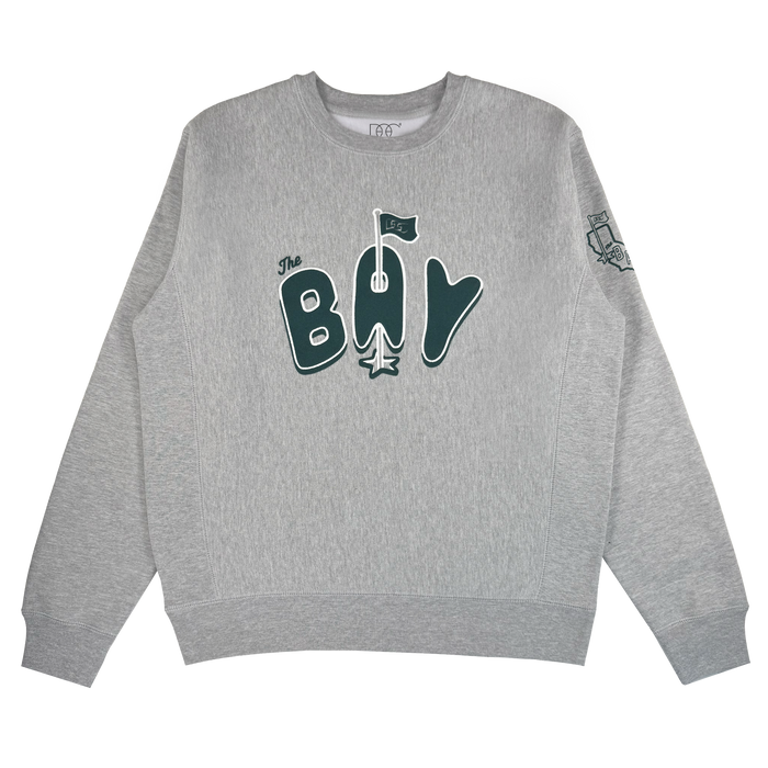 The Bay Flag Crew By DOC from Oaklandish is a heather gray heavyweight crewneck with "The Bay" in dark green, a stylized flag above the “A,” and a small embroidered sleeve graphic. Background is plain white.