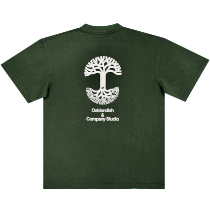 Certainly! Here’s the rewritten sentence using your product data: The Oaklandish East Bay Tee features a dark green color and a striking large white tree graphic with roots encircling a cityscape. Centered beneath the design on the back is the text "Oaklandish & Company Studio" in white. This exclusive Chaz Bear t-shirt is part of a special Toro y Moi collaboration with Oaklandish.