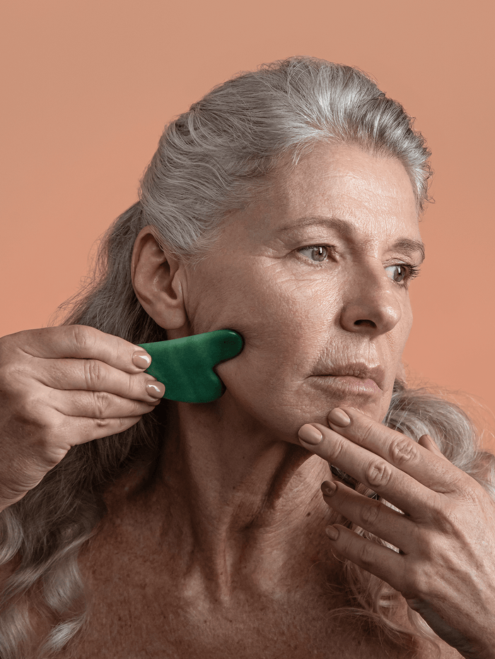 Woman using jade gua sha facial lifting tool to sculpt jawline