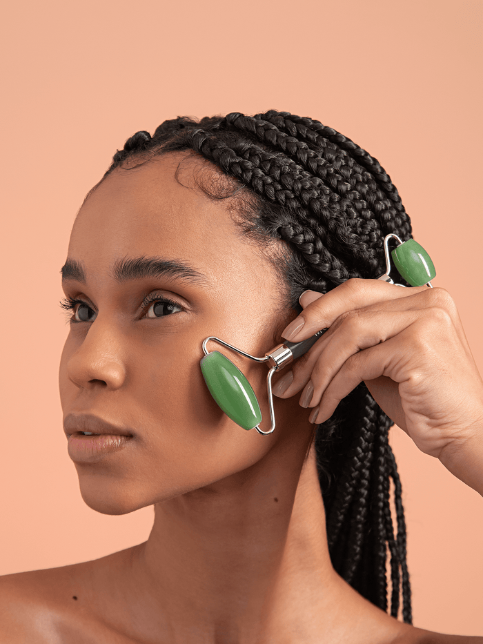 Model using jade facial roller to smooth out fascia on cheeks