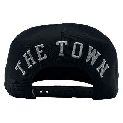 The rear view of "The Town Aft Snapback" by Oaklandish features "THE TOWN" prominently embroidered in large white letters. The hat's adjustable snapback closure, a small label tag on the side, and an embroidered Oaklandish tree logo are also visible.
