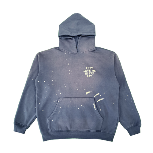 Introducing the They Love Me Hoodie By Doc from By DOC—a vintage-inspired blue men’s pullover hoodie accented with distinctive white paint splatters and a practical front pocket. Crafted from heavyweight fleece, this relaxed-fit hoodie sports a drawstring-free hood for effortless comfort. The left chest features “THEY LOVE ME IN THE BAY.” printed in white, adding a unique touch to its laid-back style.