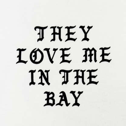The They Love Me LS Tee By Doc by By DOC features bold, black gothic-style text that reads “THEY LOVE ME IN THE BAY,” centered and evenly spaced across three lines on a crisp white heavyweight cotton long sleeve t-shirt. Designed with men’s sizing, it combines standout style with exceptional comfort.