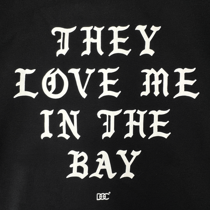White Gothic-style text on a black background reads: “THEY LOVE ME IN THE BAY.” Centered beneath the statement, a small decorative By DOC logo enhances the classic streetwear aesthetic. Crafted as part of The Bay Collection, the They Love Me Zip By Doc from By DOC delivers iconic style to your wardrobe—perfect for layering with your favorite heavyweight fleece or zip-up hoodie.