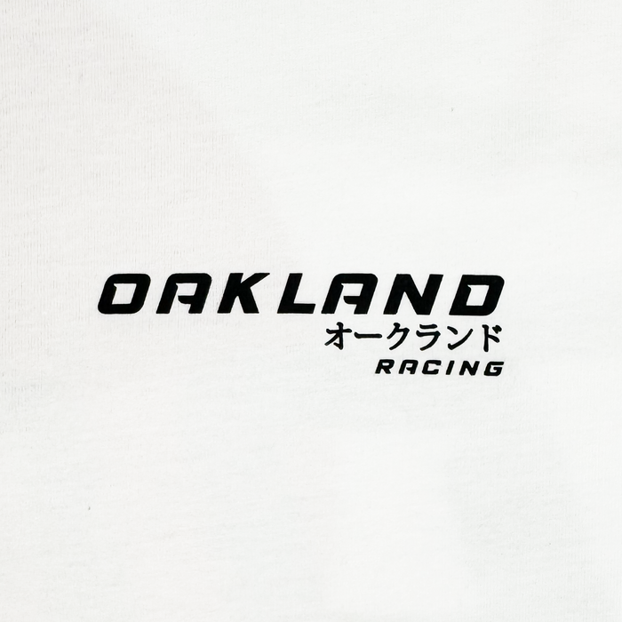The Tuner LS Tee from Oaklandish is a white, 100% cotton long sleeve shirt with bold black "OAKLAND" in caps and Japanese katakana "オークランド." Below, "RACING" appears in smaller letters, slightly tilted right. It offers a classic fit with a modern and simple design.