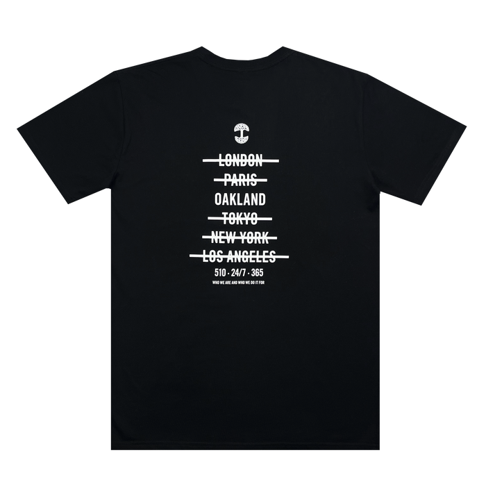 The Oaklandish "Who We Are and Who We Do it For Tee" is a 100% cotton, classic fit T-shirt with white text in a minimalist design. The text features a small anchor graphic at the top, followed by city names with lines through them: "London, Paris, Oakland, Tokyo, New York, Los Angeles." Below the cities is the text: "510-247-365".