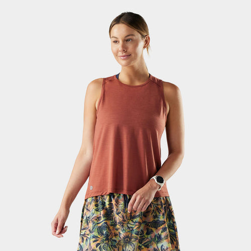 Woman wearing a rust-colored tank top and floral shorts on a white background