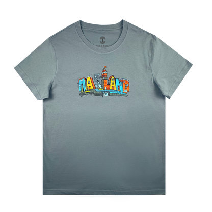 The Oaklandish Women's Blockletters Tee is a gray cotton shirt with "OAKLAND" in bold, colorful cartoon-style letters featuring city elements and skyline details, all above a subtle shadow graphic.