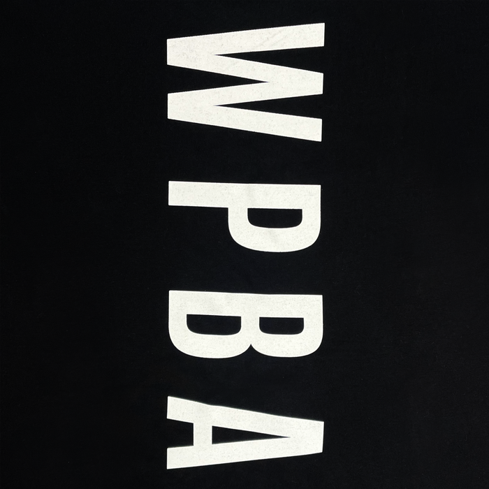 The WPBA Core LS Tee by Oaklandish features a black background with bold, white vertical letters "WPBA" arranged from top to bottom in the center of the design, symbolizing the empowerment of women's sports through the Women's Premier Basketball Association.