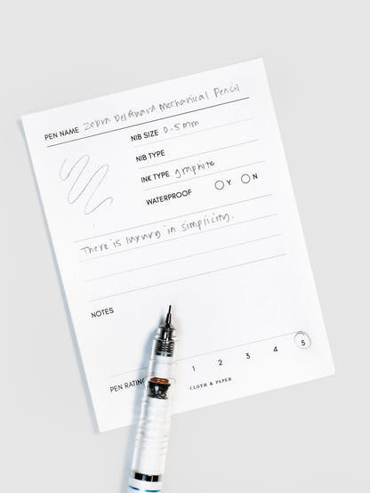 Pencil resting on a pen test sheet displaying a writing sample detailing the pencil's specs.